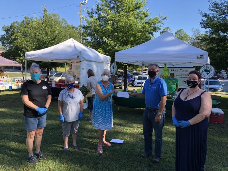 Simpsonville Farmers Market committee member Dianne Carson presents City of Simpsonville Mayor Paul Shewmaker with a $1,000 check towards a new sign for Harmony Garden, a community garden staffed by volunteers, at the Farmers Market on June 13, 2020. Lef