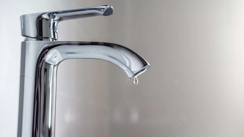 Faucet with a drop of water against a white sink - stock photo