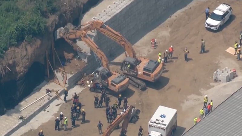 A construction worker was taken from this scene in critical condition after a concrete retaining wall under construction fell on him, knocking him down and burying him under dirt and debris.