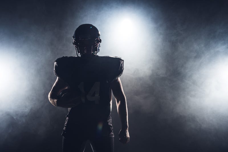 dark silhouette of football player with ball against white smoke