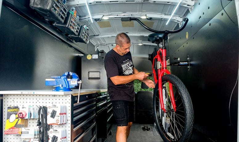 Worker stands and fixes bicycle inside high-roof Ford Transit van