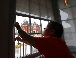 Brian Lambert, owner of Scoops, a coffee and sweets shop, opens up the windows of his business across the street from the Forsyth Courthouse as he gets ready to reopen next week in Forsyth, Ga. (Curtis Compton/tlanta Journal-Constitution via AP)