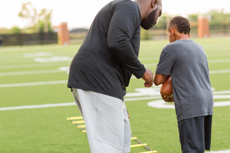 A man coaches a young football player on how to carry the ball