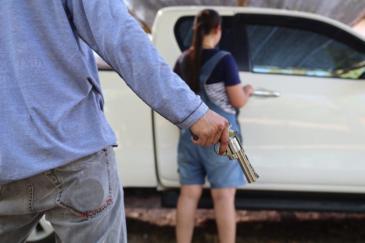 Criminal or Bandit wear black mask and black clothes, he open car door and use gun point to woman in car for trying to rob money and hurting her.