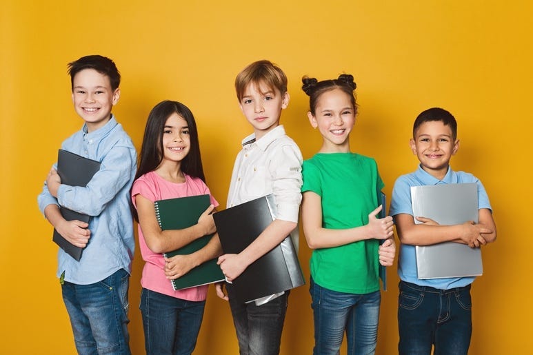 School kids with notebooks, standing in row and looking at camera over yellow background