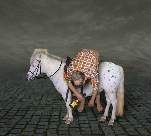 The drunk man with a bottle of rum is lying across the horse saddle.