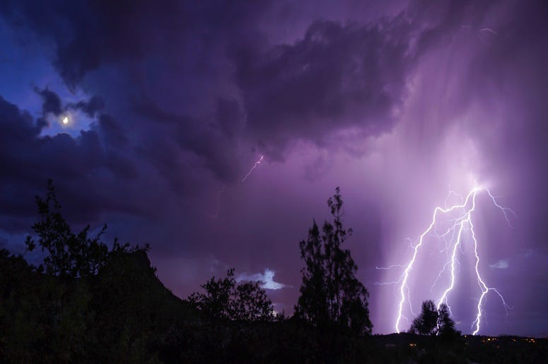 The moon is still visible as a lightning storm moves in.