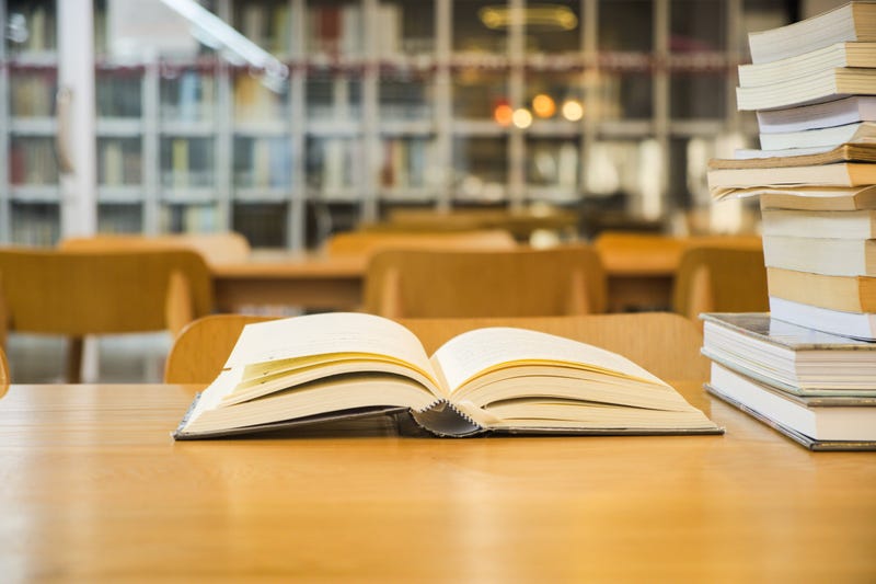 Books placed on a wooden table on blurred bookshelf in library room background
