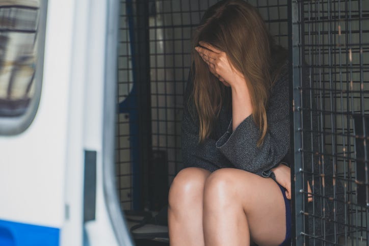 Female criminal sitting in police van and covers her face with her hand.