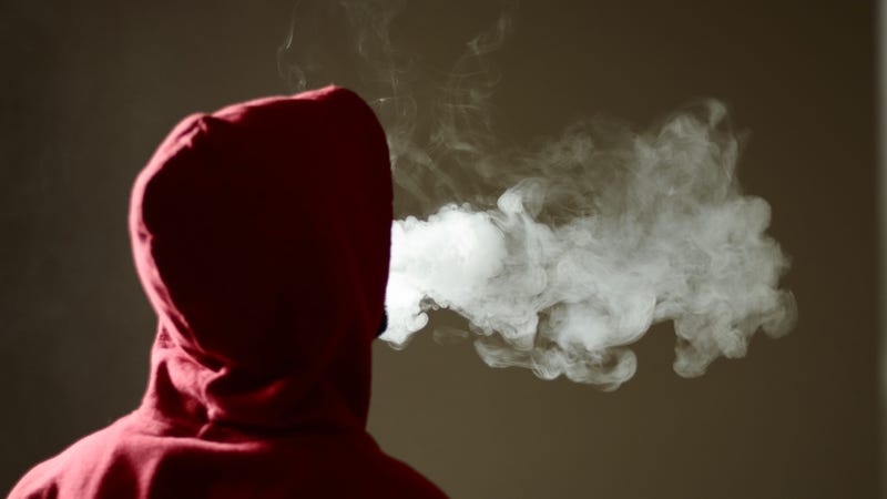 Young male in red hoodie vaping smoking, exhales thick vapor.