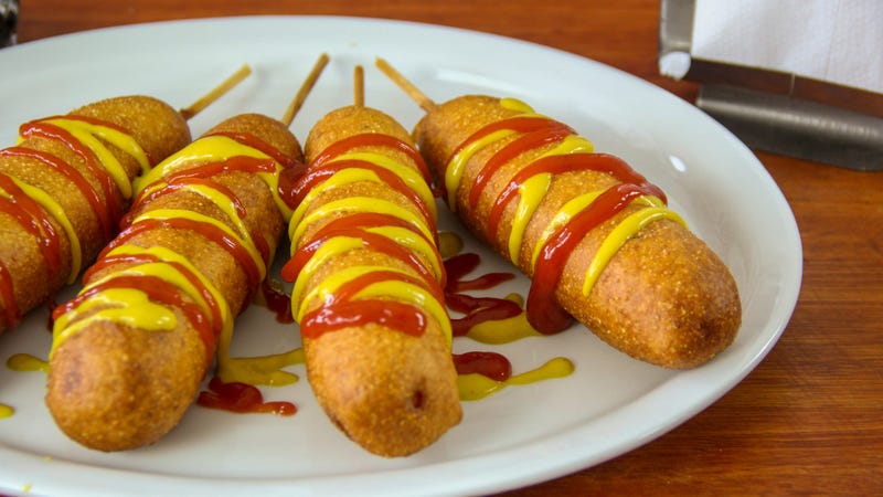 Golden corn dogs in a plate with ketchup and mustard on top