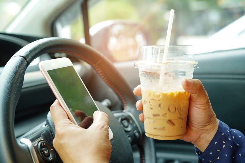 Woman trying to drive while texting and holding coffee