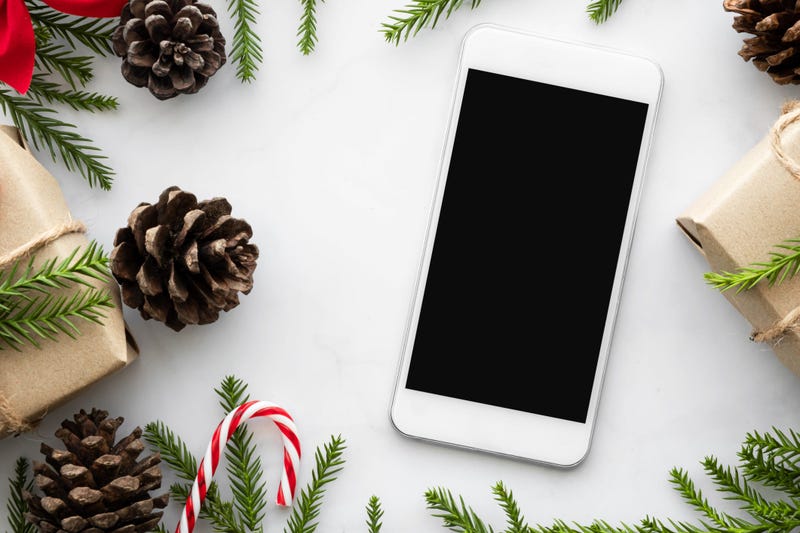 Smartphone with blank screen is in the middle of white marble table with Christmas decorations. Top view, flat lay.