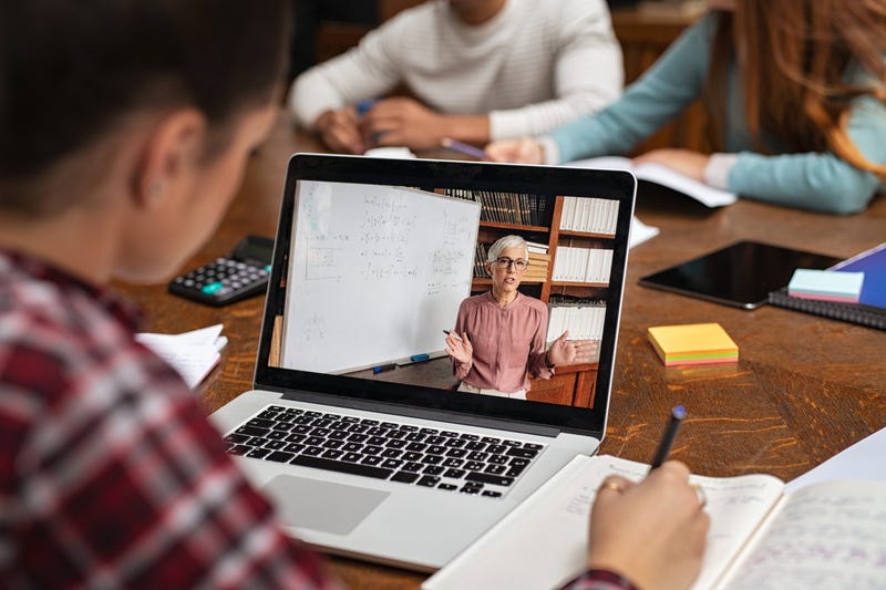 Teacher explaining lesson in video call while girl taking notes.