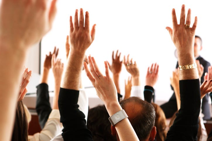 Big audience of people raising their hands to vote in favor of some topic.