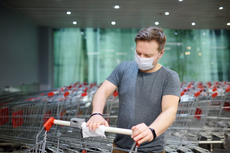 Man in face mask disinfects grocery shopping cart