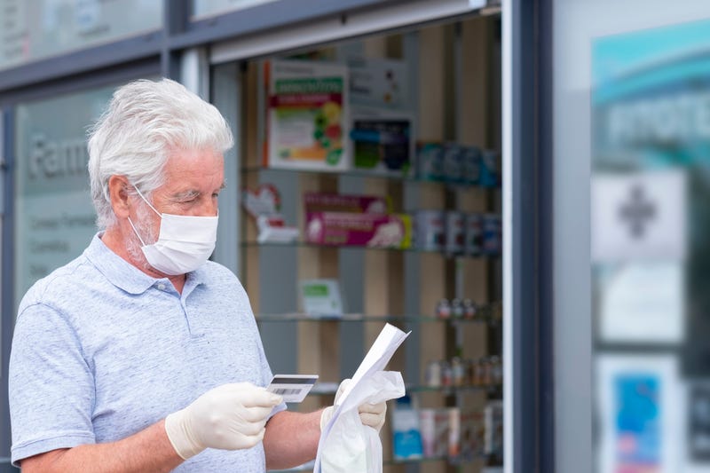 Elderly man with mask and protective gloves leaves the chemist's shop with medicines and instructions. 