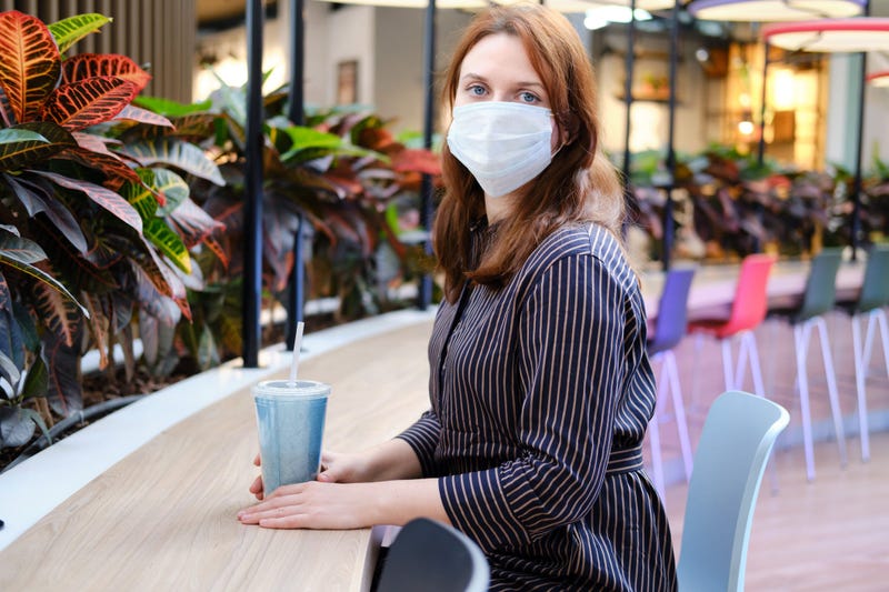 Portrait of a sad woman in a medical mask at a table in a cafe. The face of a girl with influenza coronavirus in a restaurant