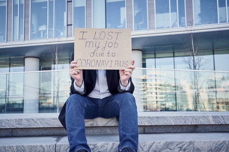 A man holds sign "I lost my job because of coronavirus." as he sits Male sitting on stairs of building at his  former place of work in the business center.