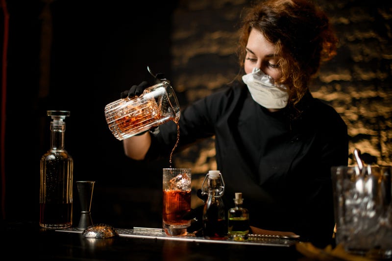 Woman wears glove and face mask while bartending