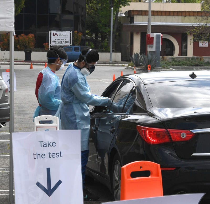 Workers wearing personal protective equipment gather the tests administered from people's cars as Mend Urgent Care hosts a drive-thru testing.