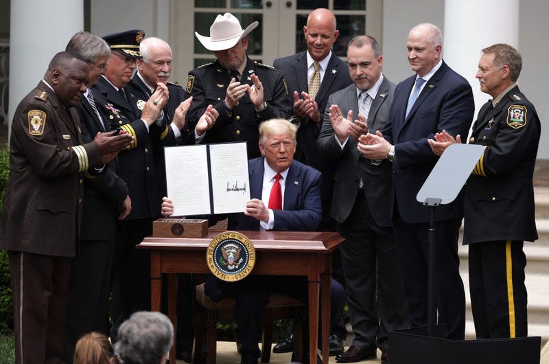 Surrounded by members of law enforcement, U.S. President Donald Trump holds up an executive order he signed on “Safe Policing for Safe Communities” during an event in the Rose Garden at the White House.