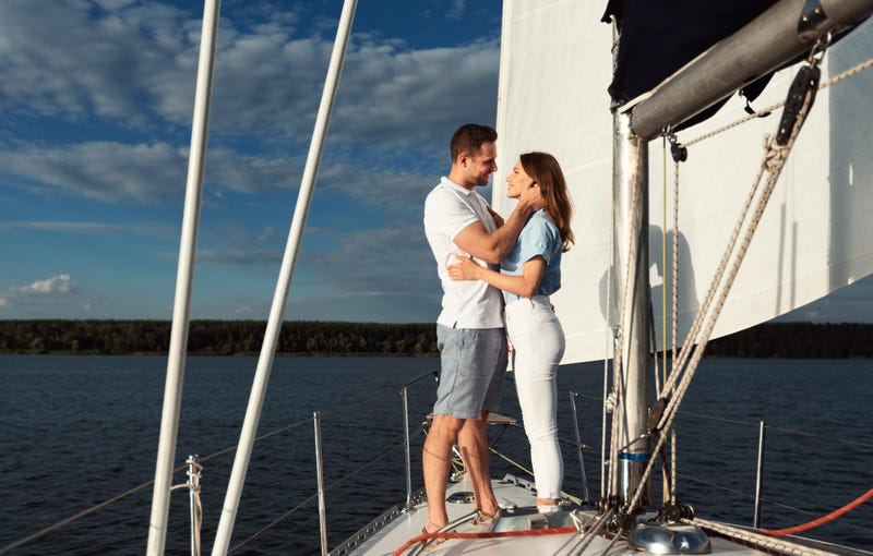 Romantic Date On Yacht. Loving Couple Embracing Standing On Sailboat Deck Enjoying Honeymoon Sailing On River Outdoor.
