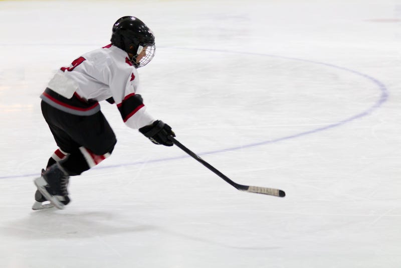 A little boy in a full hockey uniform skates and handles a puck with his stick