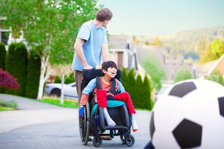 Caucasian father helping disabled son in wheelchair play soccer