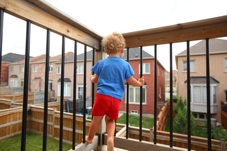 Little boy standing on the balcony (patio) above the ground and trying to climb on balcony railing. House living and child-proofing