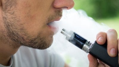 Man vaping exhales a cloud of vapor