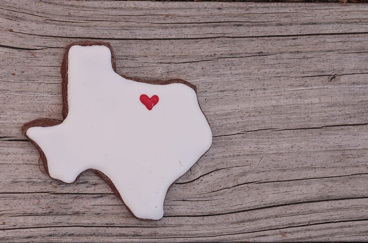 Texas shaped sugar cookie with white icing and a red heart on a rustic wood table.