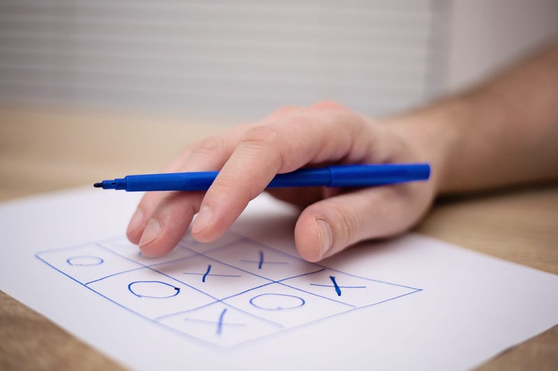 male adult hand holding blue pen above a paper with a tic-tac-toe game