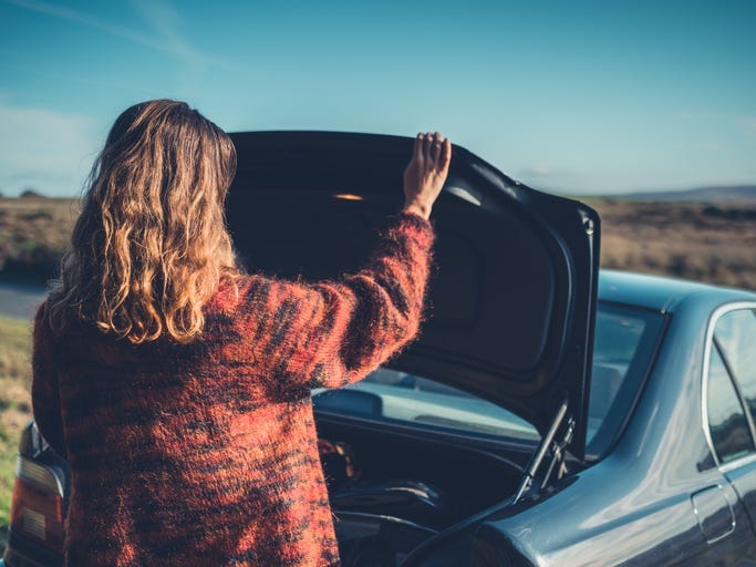 A young woman is opening the trunk of her car in the wilderness