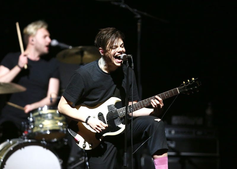 Yungblud plays guitar on stage with his trademark pink socks and giant smile.