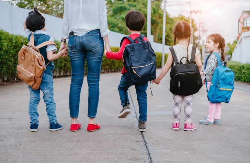 Motherl and kids holding hands going back to school with backback.