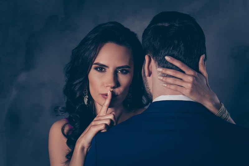 Couple in romantic embrace, woman shushes the viewer