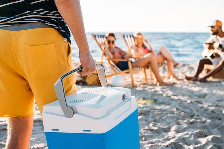 A man carries a cooler on a beach.
