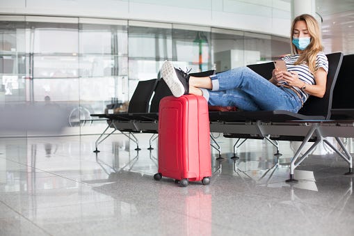 Woman waiting at empty departure gate, wearing protective face mask