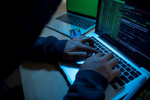 A person in a black sweatshirt types code on a laptop.