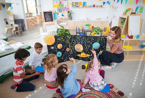 A group of Kindergarten children gathered around a teacher on the floor