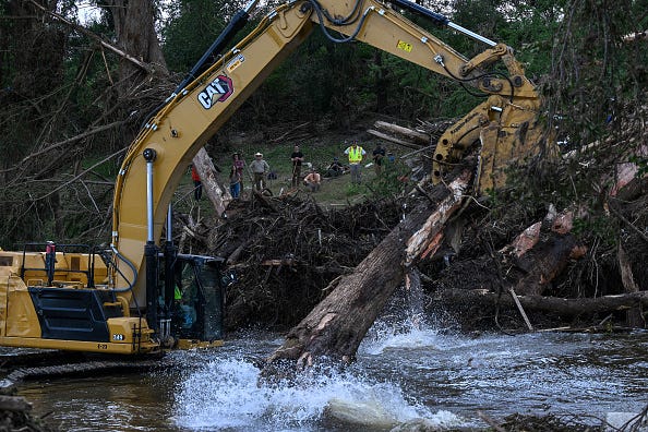 an excavator removes trees damaged in the Central Texas floods along the Guadalupe River as they search for victims on July 9, 2025 in Center point, Texas. Over a 100 people have died in the Central Texas floods and over 160 people remain missing