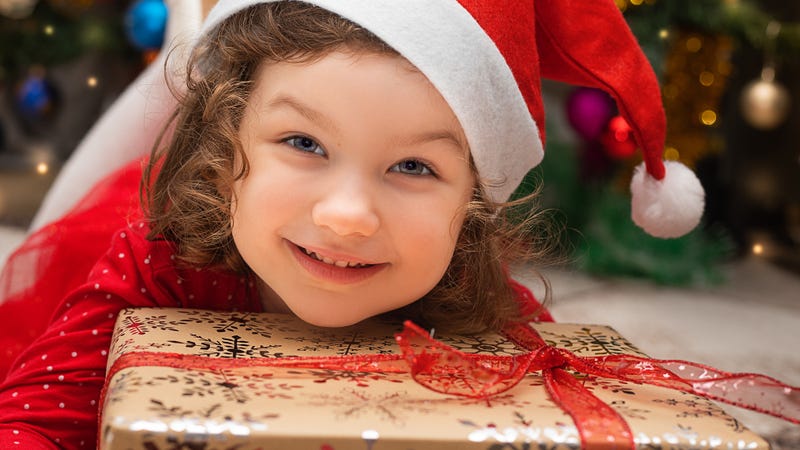 A young girl in Santa hat smiles with her Christmas present
