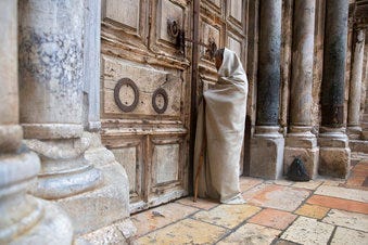 A Christian worshiper stands at the closed door of the Church of the Holy Sepulchre, believed by many Christians to be the site of the crucifixion and burial of Jesus Christ, in Jerusalem, Friday, April 10, 2020. (AP Photo/Sebastian Scheiner)