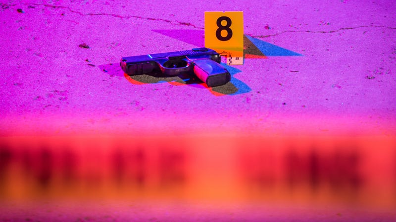Black handgun on the pavement in a crime scene, marked with an evidence marker - stock photo