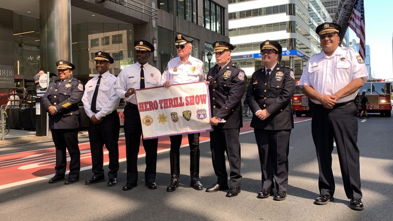 Police and fire officials in Center City hold a banner promoting the upcoming Hero Thrill Show.