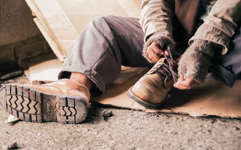 Homeless man wearing sweater and cloth gloves with sitting on cardboard