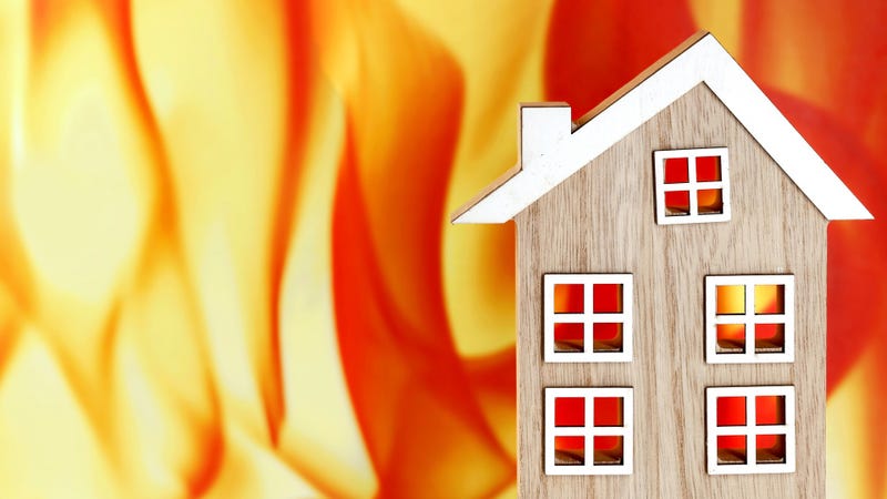Wooden model house in front of a fire flames background - stock photo