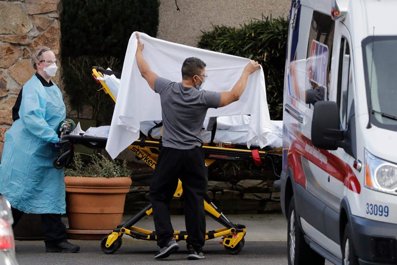 A staff member blocks the view as a person is taken by a stretcher to a waiting ambulance from a nursing facility where dozens of people are being tested for Wuhan coronavirus.