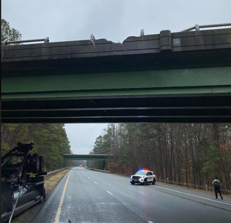 A damaged overpass, an overturned tractor-trailer, and a police car with its lights on